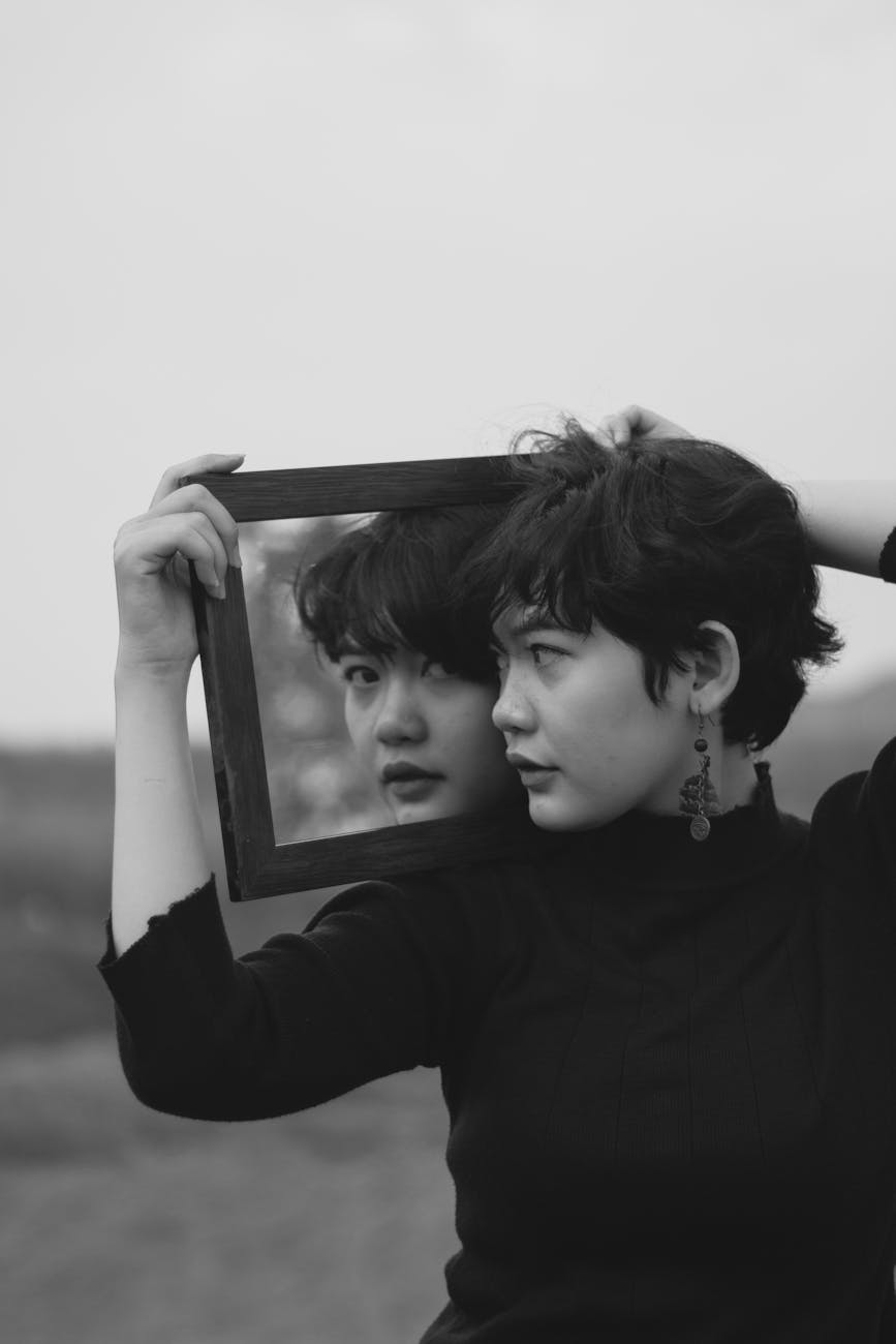 grayscale photo of woman holding a mirror